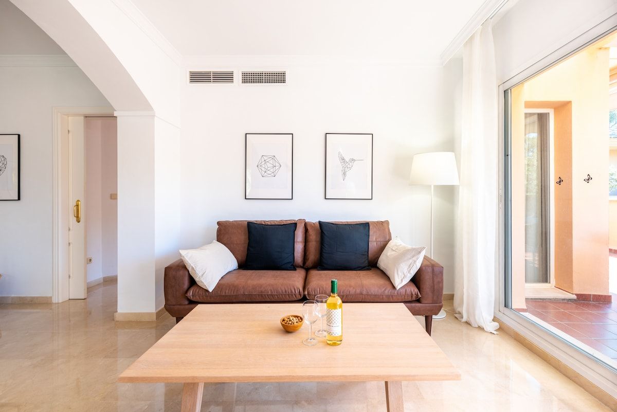 A modern living room with a brown leather sofa, a wooden coffee table, and two framed artworks on the wall.