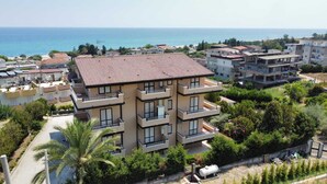 A multi-story building with balconies, surrounded by greenery and a coastal view. - The Riace Palms 3 (Riace Marina)