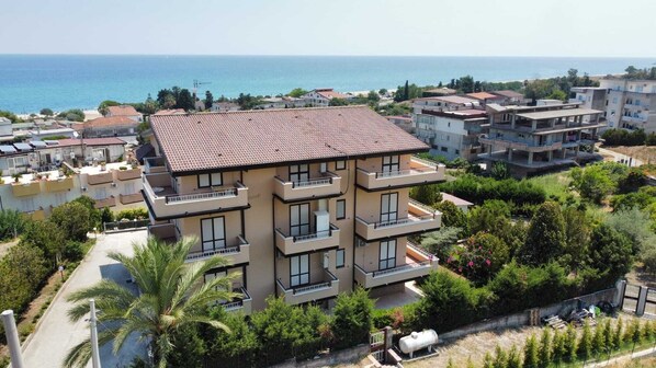 A multi-story building with balconies, surrounded by greenery and a coastal view.