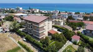 A multi-story residential building with balconies, surrounded by greenery and a view of the sea. - The Riace Palms 3 (Riace Marina)