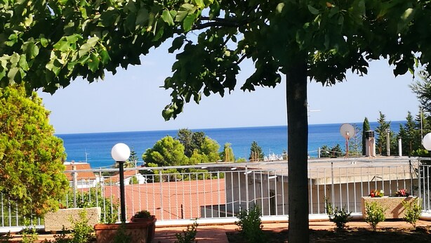 A residential area with a view of the sea, a fenced garden, and a building with satellite dishes. - The Riace Palms 3 (Riace Marina)