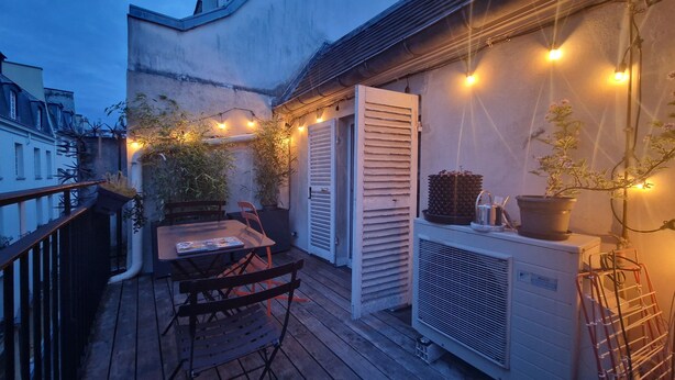 A wooden deck with a table and chairs, a potted plant, and a white air conditioning unit.