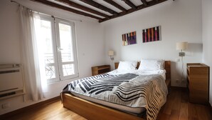 A bedroom with a wooden bed, two bedside tables, a window with curtains, and two wall-mounted lamps.