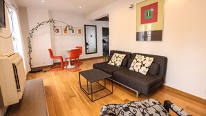 A modern living room with a sofa, a coffee table, and a dining area with red chairs.