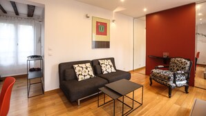A modern living room with a sofa, armchair, and coffee table. There is a small side table and a red accent wall.