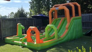 An inflatable play structure in a backyard with a wooden fence and a blue umbrella in the background.