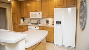 A modern kitchen with wooden cabinets, a white refrigerator, a microwave, and a stove.