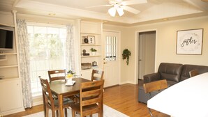 A dining area with a wooden table and chairs, a white rug, and a ceiling fan.