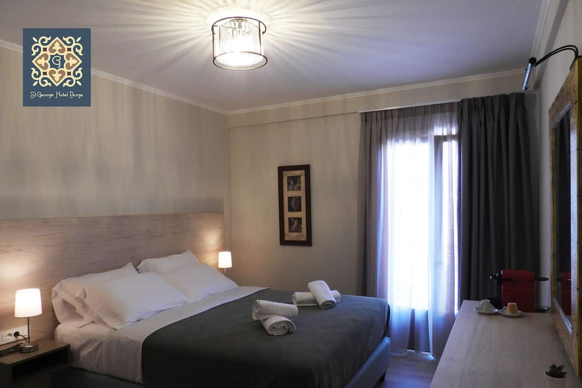 A hotel room with a large bed, two bedside lamps, a desk with a chair, and a window with curtains.