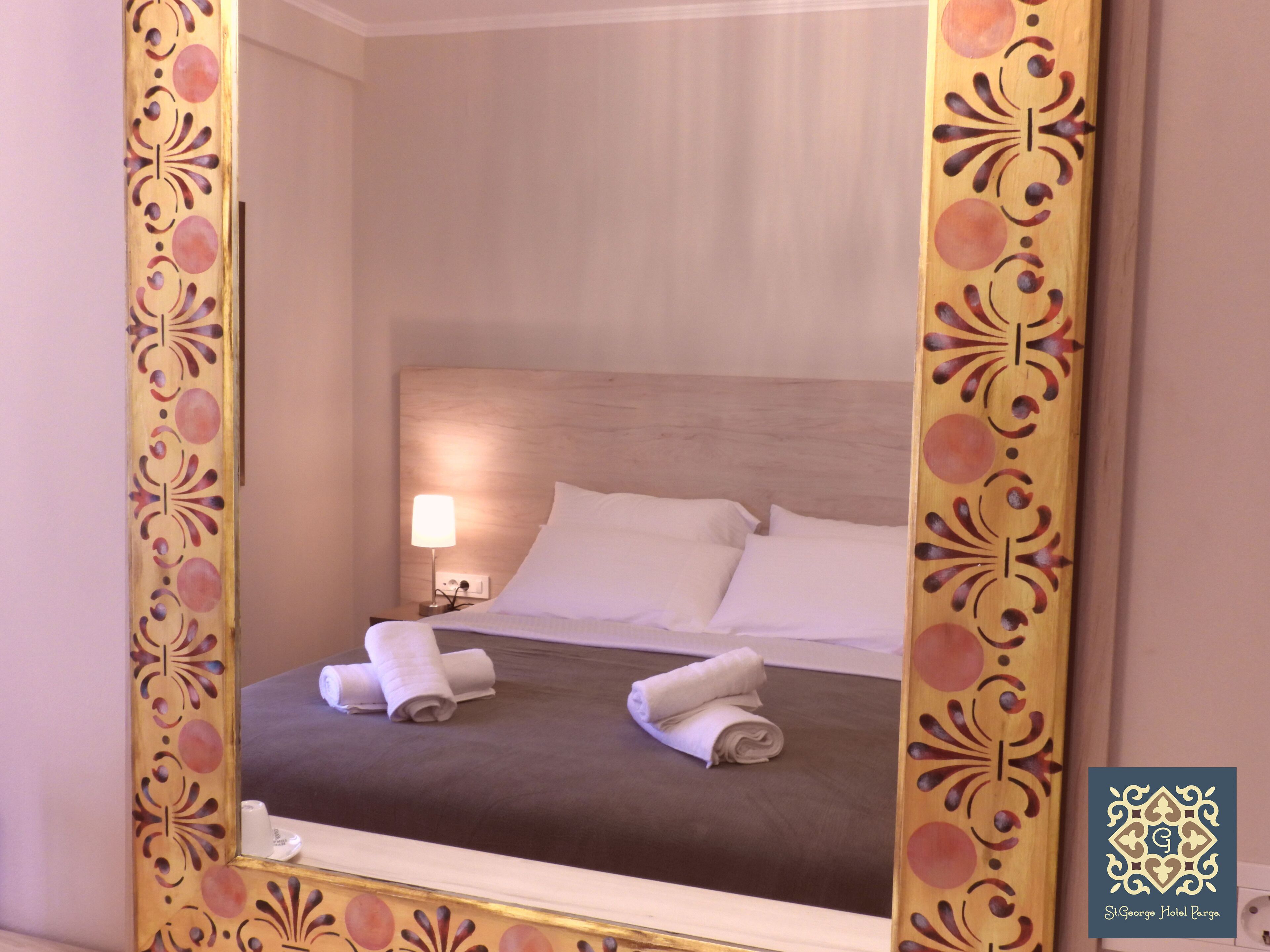 Ein Hotelzimmer mit Bett, Kissen, einem Nachttisch mit Lampe und einem Spiegel mit Zierrahmen.