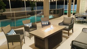 An outdoor seating area with wicker furniture, a fire feature, and a view of a swimming pool at night.