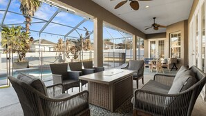 A covered outdoor area with wicker furniture, a pool, and a view of palm trees.