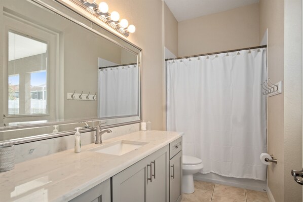 A bathroom with a large mirror, two sinks, a toilet, and a shower curtain.
