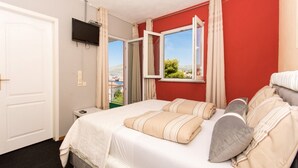 Ett hotellrum med en säng, en tv som är monterad på väggen, ett fönster med gardiner och utsikt  över omgivningen.