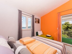 Une chambre d’hôtel avec un lit, un fauteuil vert, une fenêtre avec des rideaux et un balcon donnant sur un paysage verdoyant.