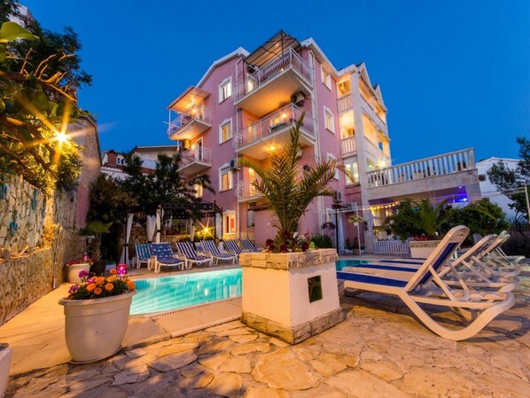 A multi-story hotel with a pool, outdoor seating, and a stone wall.