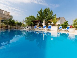Une piscine à l’eau bleue, entourée de chaises longues et d’arbres.