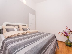 Una cama bien hecha con ropa de cama a rayas, una puerta blanca y un jarrón con flores en el suelo.