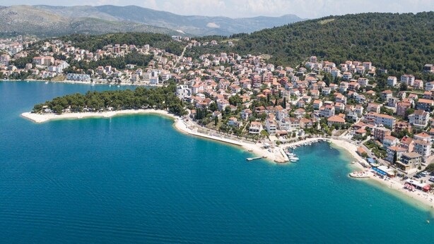 An aerial view of a coastal town with dense housing, a sandy beach, and a small peninsula with a pier.