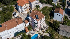 An aerial view of a residential area with multiple buildings, including a large building with a swimming pool and sun loungers.
