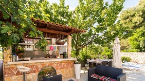 An outdoor seating area with wicker furniture, a stone bar, and a view of trees and hills.