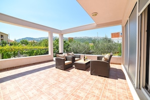 Un patio techado al aire libre con mobiliario de mimbre y vistas a la vegetación y montañas.