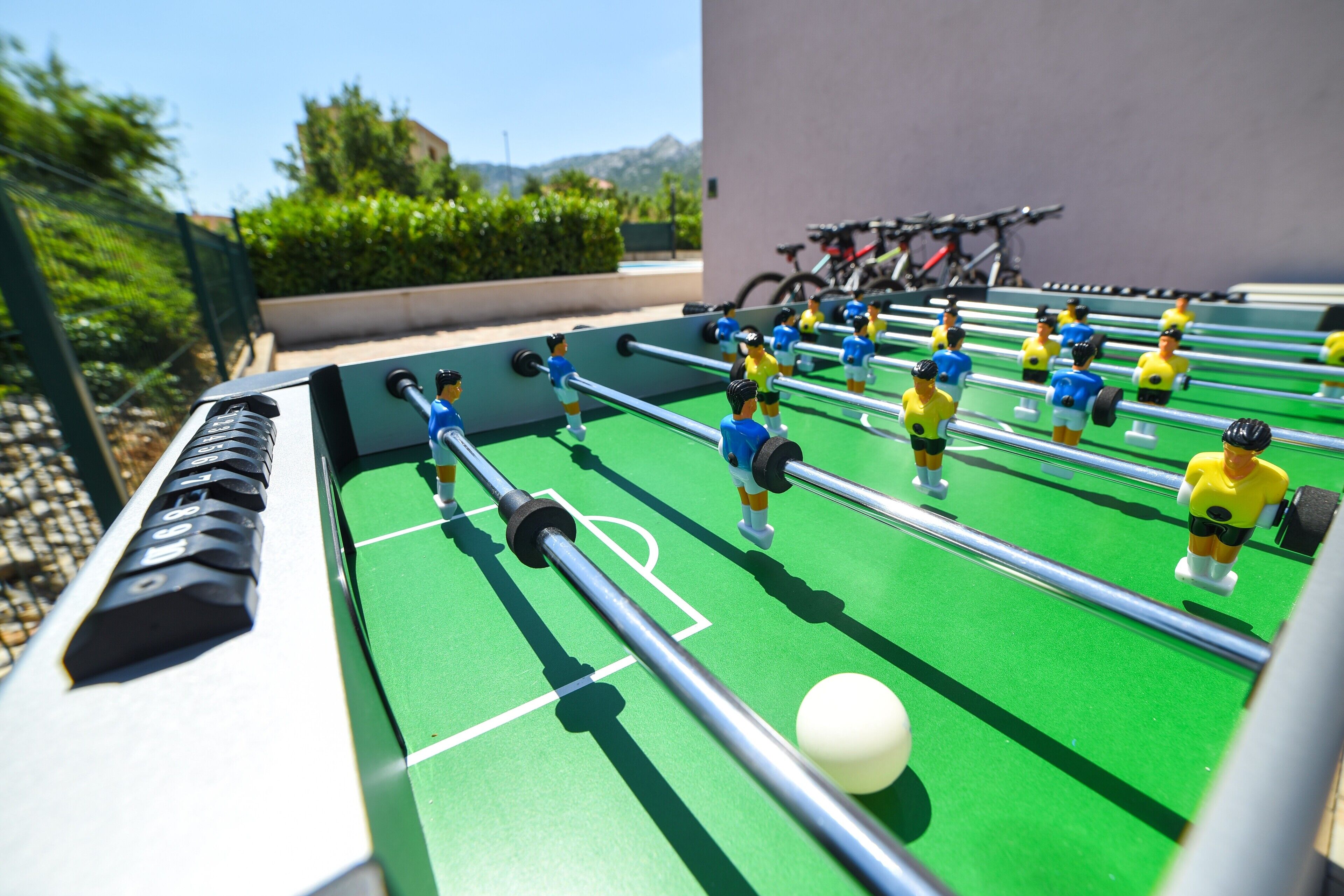Ein Kicker mit Spielfiguren in blauer und gelber Uniform, vor einem grünen Spielfeld mit einem weißen Ball.