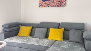 A grey sectional sofa with a quilted grey cover, two yellow and one grey patterned pillow, and a small white side table. - Apartment Alba - Three Bedroom Apartment with Loggia (Split)