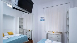 Ein Hotelzimmer mit zwei Betten, einem Fernseher, einem kleinen Schreibtisch und einem Fenster mit Vorhängen.