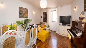 Ein Wohnzimmer mit Essbereich, einem Klavier, einem Fernseher und einem Gemälde an der Wand.
