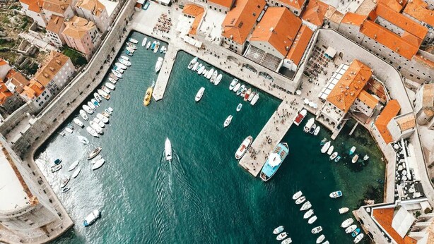 Eine Luftaufnahme eines Yachthafens mit vertäuten Booten, umgeben von Gebäuden mit orangenen Dächern.