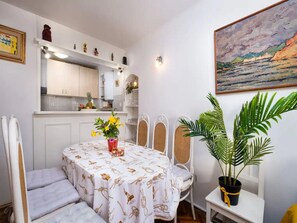 A dining area with a table set for two, a potted plant, and a kitchen in the background.