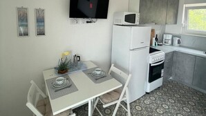Cocina compacta con microondas, estufa y lavaplatos. Hay una mesa de comedor con sillas y un ventilador de techo.