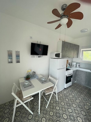 Cocina compacta con microondas, estufa y lavaplatos. Hay una mesa de comedor con sillas y un ventilador de techo.