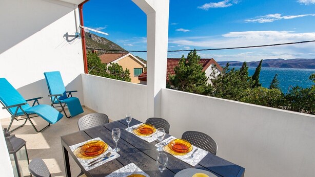A dining area with a table set for four, overlooking a scenic view of a lake and mountains. - Apartments Sun 4 You - Two Bedroom Apartment with Balcony and Sea View (Karlobag)