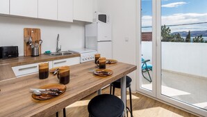 A modern kitchen with white cabinets, a wooden countertop, and a view of the outdoors through a sliding glass door. - Apartments Sun 4 You - Two Bedroom Apartment with Balcony and Sea View (Karlobag)