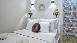A bedroom with a bed, white bedding, two wall-mounted lights, and a stone wall. - History House Moja Ti 1830 - Superior Apartment with Sauna (Senj)