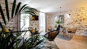 A spacious living area with a stone wall, a dining table with chairs, and a large plant in the foreground. - History House Moja Ti 1830 - Superior Apartment with Sauna (Senj)