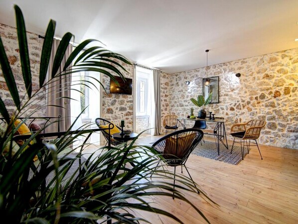 A spacious living area with a stone wall, a dining table with chairs, and a large plant in the foreground.