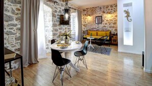 A dining area with a round table, two black chairs, a yellow sofa, and a stone wall. - History House Moja Ti 1830 - Deluxe Apartment (Senj)