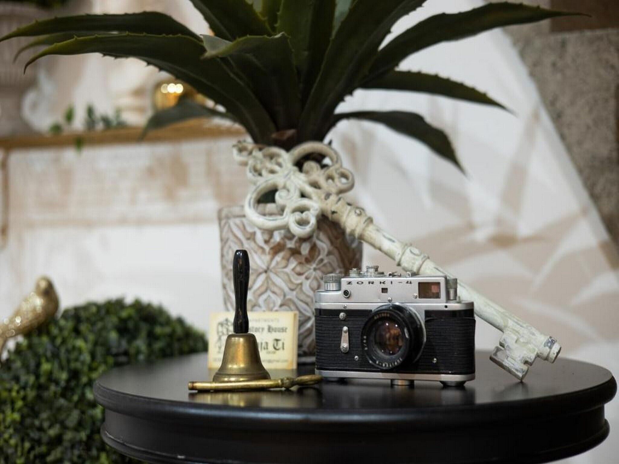 Un appareil photo ancien, posé sur une table ronde, avec une cloche et un vase décoratif.