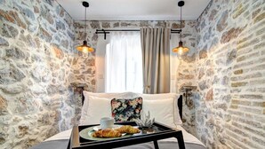 A cozy room with stone walls, a bed with a floral pillow, a tray with croissants, and two hanging lights. - History House Moja Ti 1830 - Deluxe Apartment (Senj)