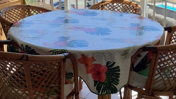 A round table with a floral tablecloth, surrounded by wicker chairs, on a balcony with a view of a park and a pool. - LE CAP D'AGDE - near sea - Appt tt confort - residence with swimming pool - Pk private (Agde)