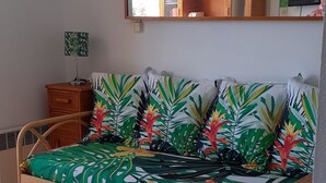 A room with a bed, a wooden side table, a green trash bin, and a wall-mounted shelf with decorative items. - LE CAP D'AGDE - near sea - Appt tt confort - residence with swimming pool - Pk private (Agde)