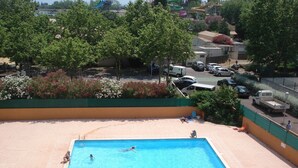 A swimming pool with people swimming, surrounded by a fenced area and greenery. - LE CAP D'AGDE - near sea - Appt tt confort - residence with swimming pool - Pk private (Agde)