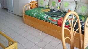 A compact living space with a kitchenette, a sofa bed with floral cushions, a television mounted on the wall, and a dining table with chairs. - LE CAP D'AGDE - near sea - Appt tt confort - residence with swimming pool - Pk private (Agde)