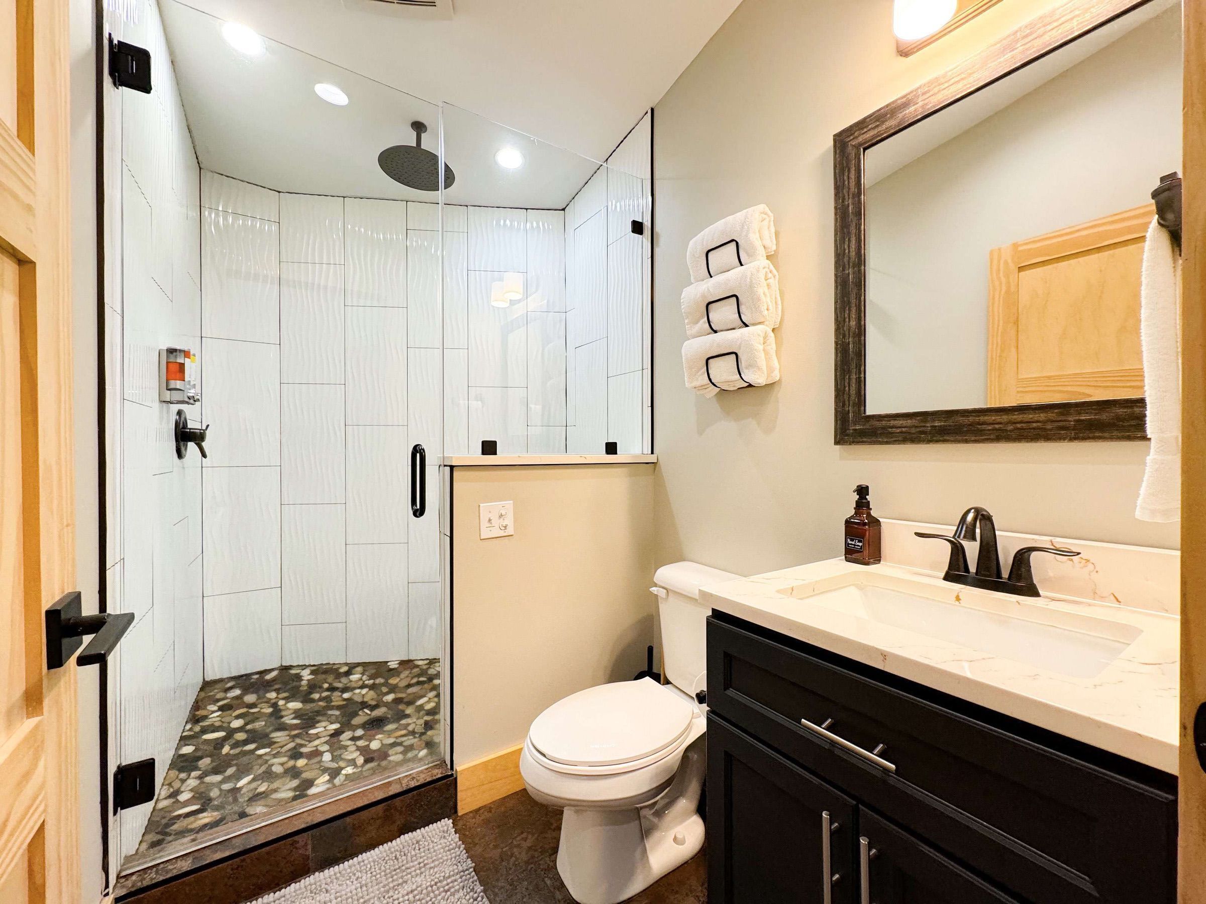 Une salle de bain moderne avec une douche à parois de verre, des toilettes, un lavabo avec un miroir et un porte-serviettes.