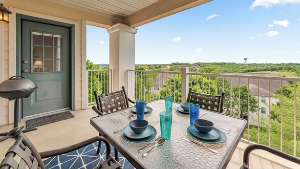 Un balcon avec une table dressée pour le dîner, une porte et une vue sur le paysage environnant.