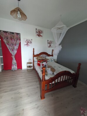 A bedroom with a wooden bed, a red curtain, a white canopy, and wall art. - Spacious studio with a terrace in Village Créole (Les Trois-Îlets)