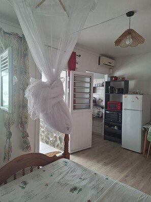 A room with a bed, a table with a menu, a kitchen area with appliances, and a window with curtains. - Spacious studio with a terrace in Village Créole (Les Trois-Îlets)
